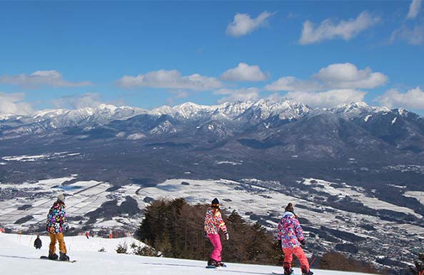 青空と雪山を背景にした女性スケートボーダー３人組